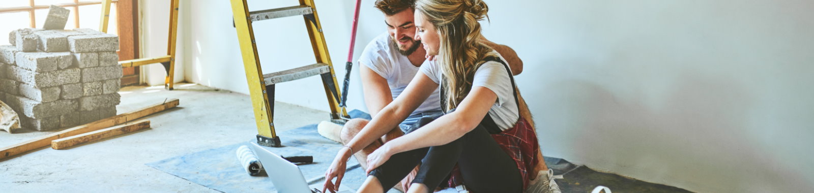 Couple sitting on the floor on computer, taking a break from house work