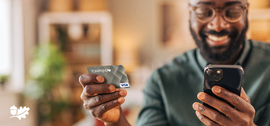 Man holding up Tompkins credit card and phone